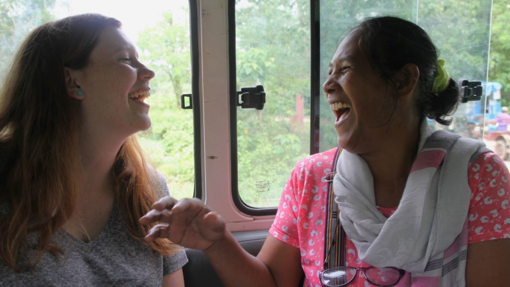 Two women facing each other on a bus laughing