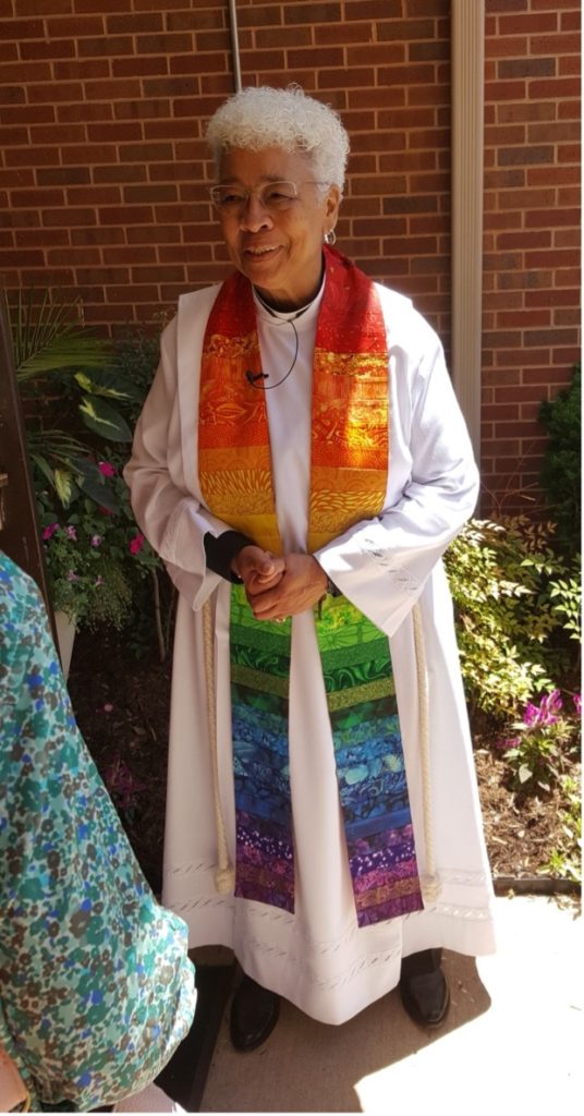 The Rev. Shug Goodlow wearing a white alb and rainbow-colored stole.